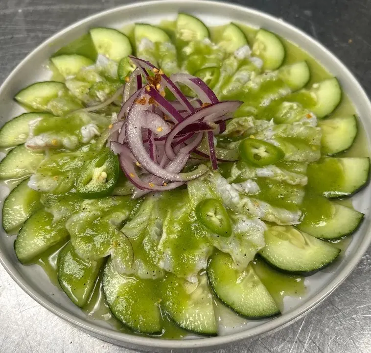 Camarón abierto en chile verde y limón, rodeado de pepino y con cebolla morada encima.