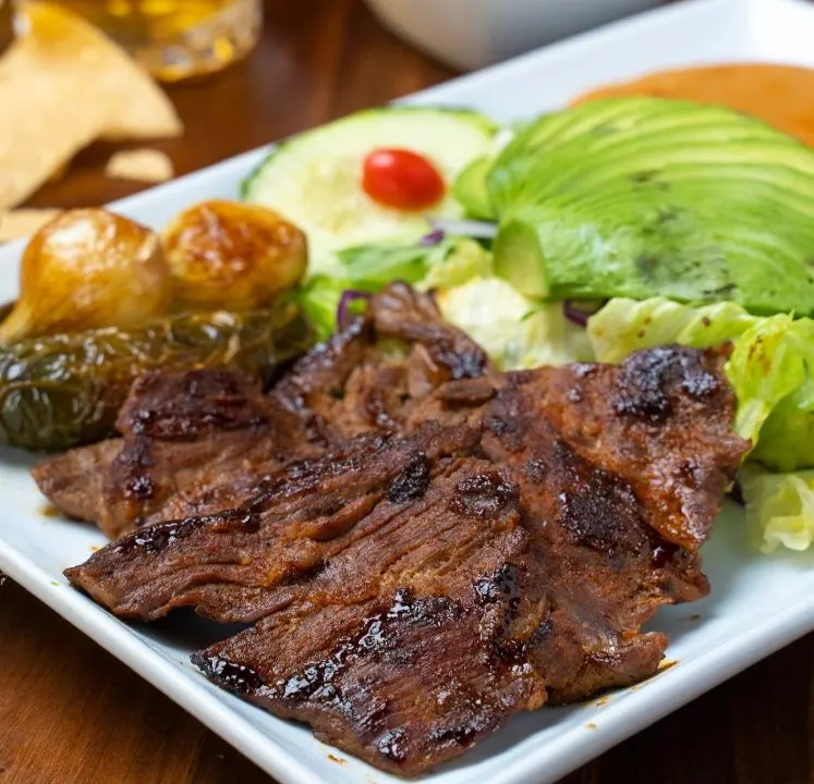 Carne asada con aguacate rebanado, chile toreado y papas.