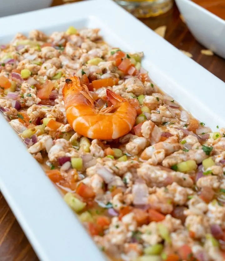 Un plato largo de ceviche de camarón con camarones cocidos enteros encima.