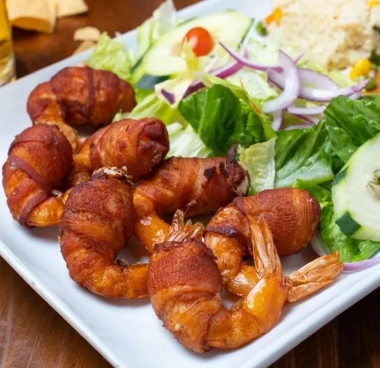 Camarones envueltos en tocino con ensalada y arroz.