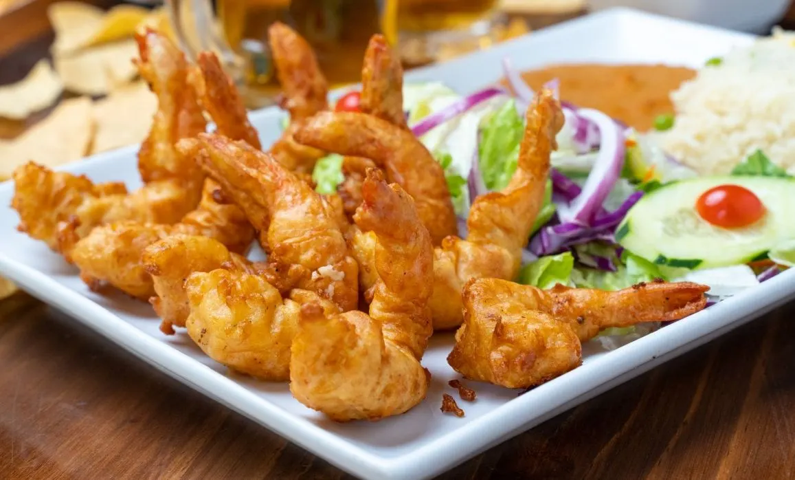 Camarones empanizados y dorados, abiertos en mariposa, con ensalada y arroz.