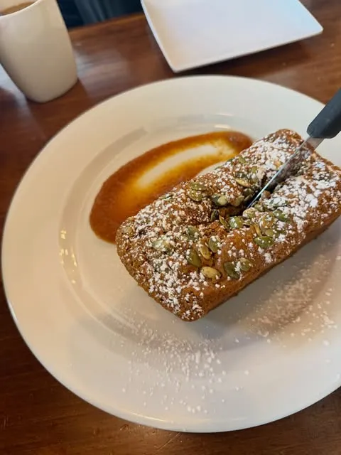 Un panecito de calabaza con pepitas y azúcar glas, con un cuchillo cortándolo.